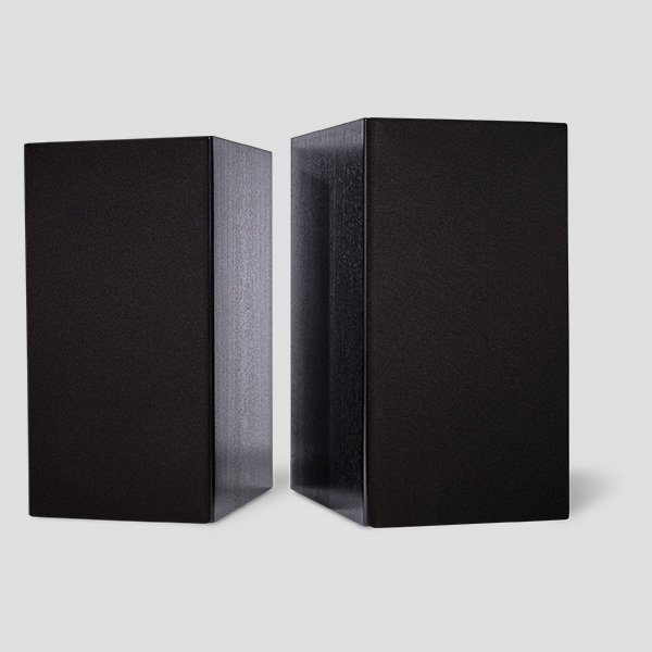A pair of Signature One monitors in black veneer with the magnetic grilles fitted, angled towards each other so the satin black side panel catches the light between them